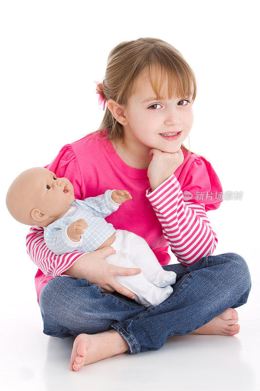 穿着粉红色衣服的年轻女孩坐在地板上，手里拿着一个娃娃