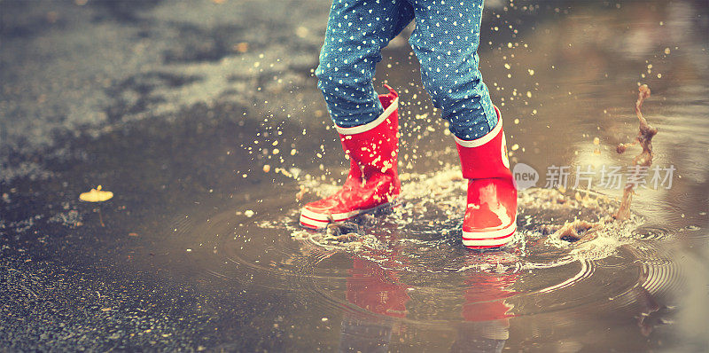穿着红色橡胶靴子的孩子的腿在水坑里跳