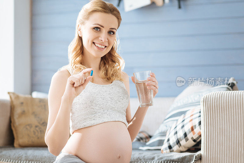 一名孕妇展示一粒药丸和一杯水