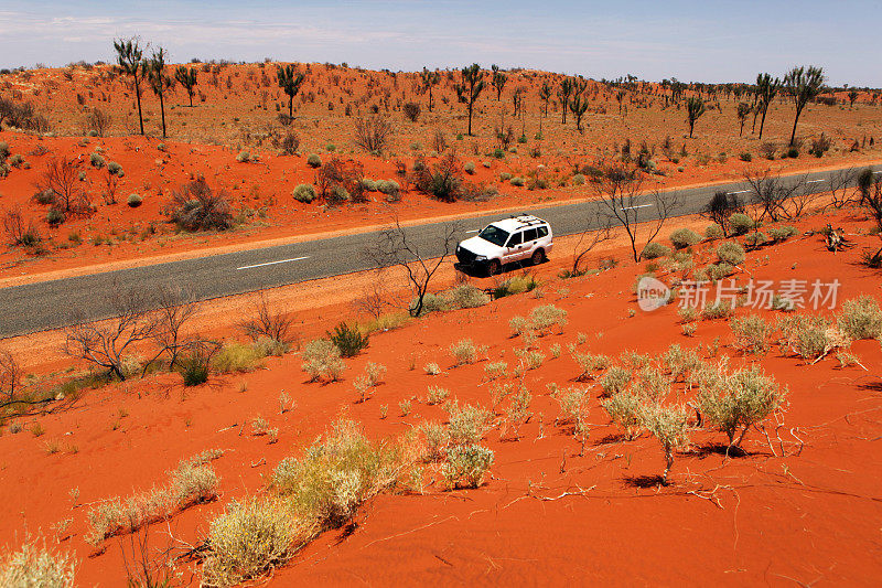 汽车行驶在红色的道路上，穿过澳大利亚内陆的风景