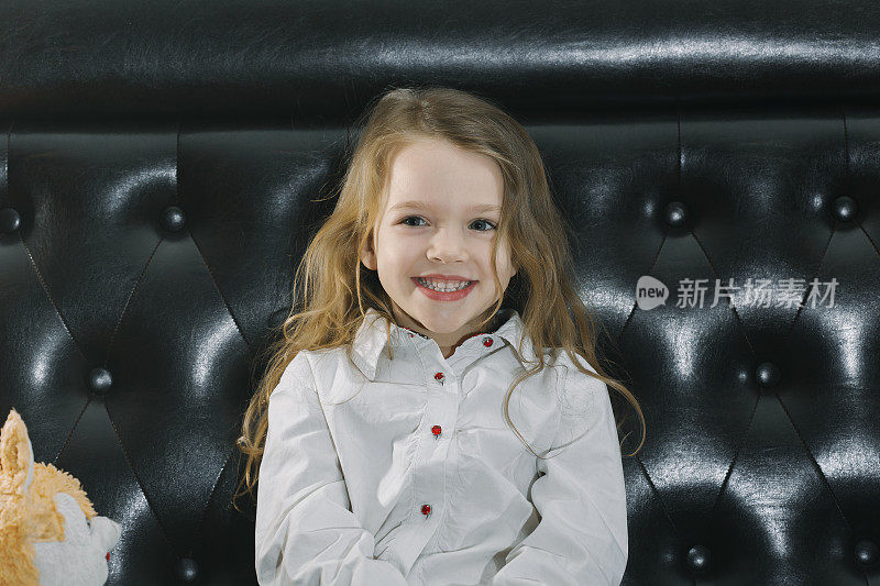 微笑的女孩坐在沙发上与填充玩具