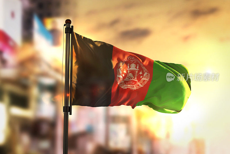 在日出的背光下，城市模糊的背景下的阿富汗国旗