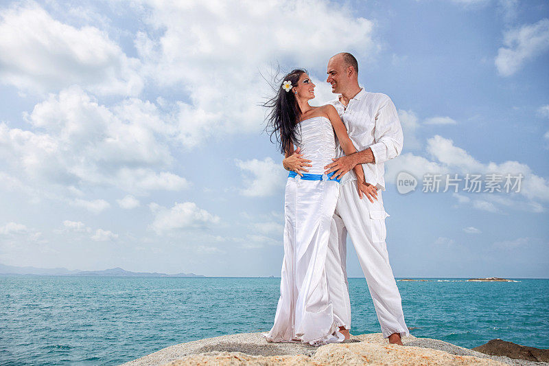 一对深情的新婚夫妇站在海边的一块岩石上。