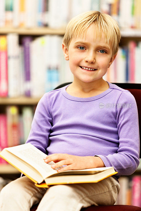 微笑的年轻读者在图书馆享受她的书