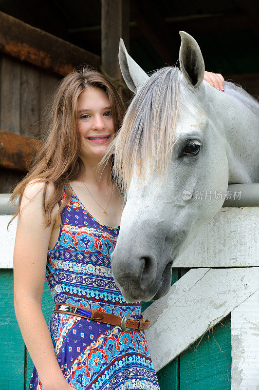 年轻女孩和白马在马厩门口