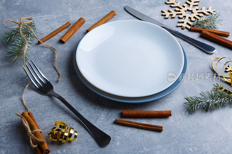 桌子上放着一个盘子，上面有刀叉和肉桂棒、圣诞树树枝和雪花做的装饰。
