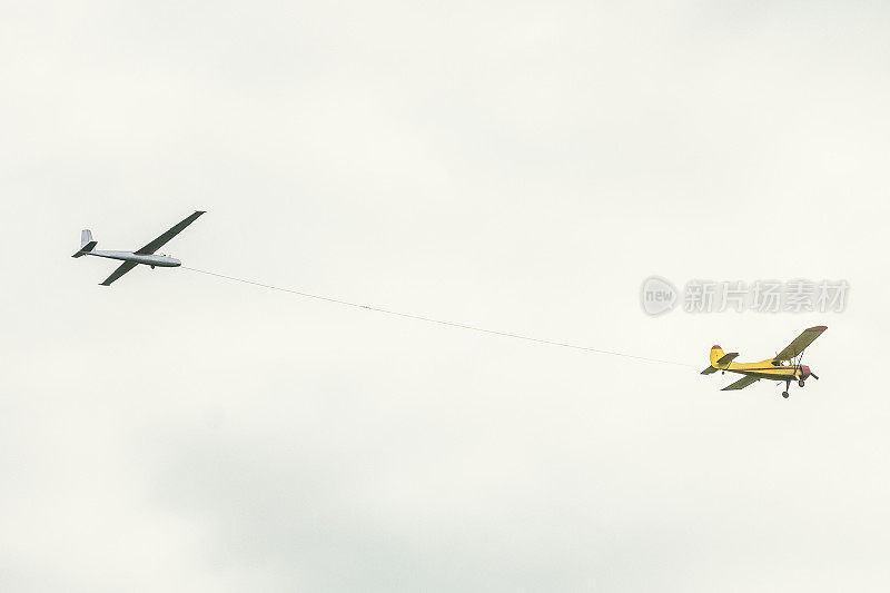 黄色的小型轻型运动飞机在空中飞行，拉着一根绳子的滑翔机飞机