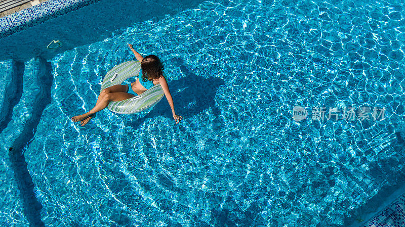 鸟瞰图美丽的女孩在游泳池从上面，游泳在充气圈甜甜圈和有乐趣的水在家庭度假