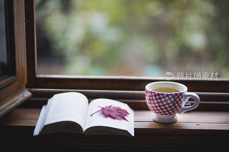 一本翻开的书，有一片红叶，还有一杯茶