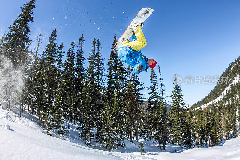 在森林和山脉的背景下，滑雪自由人从雪坡上跳下来