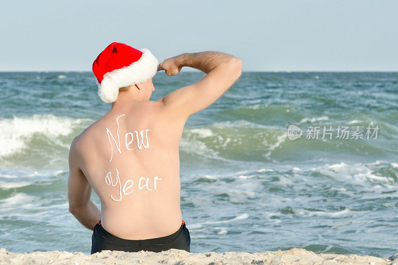 戴圣诞老人帽的男人望着远方。在背面题词新年。海岸。