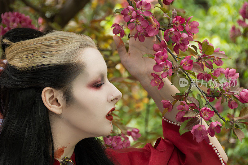 年轻女子在吸血鬼化妆，侧面特写，与深粉红色的春天花朵。
