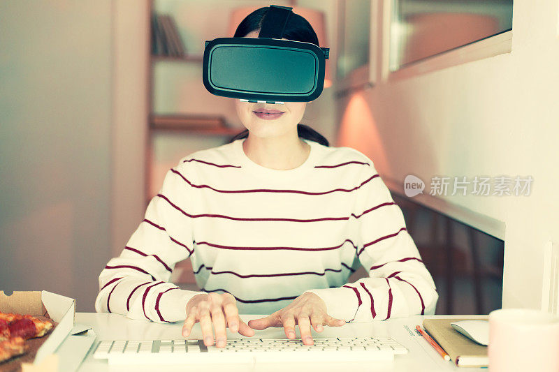 年轻女子在电脑上工作时使用虚拟现实头盔