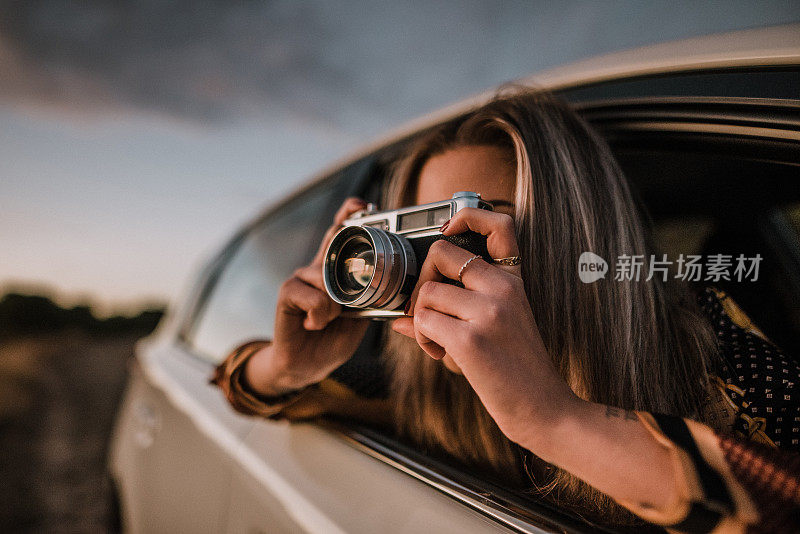 一名年轻女子在车窗外用老式相机拍照