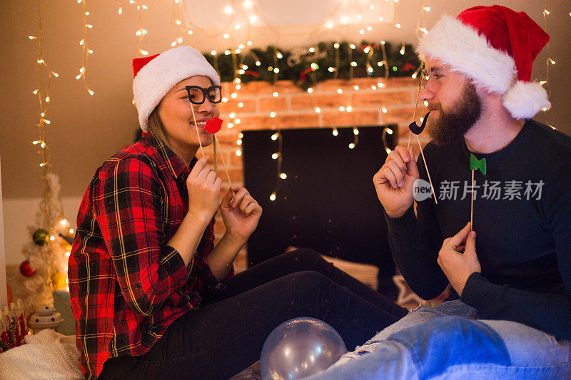 一对相爱的年轻情侣坐在壁炉和装饰精美的圣诞树旁，享受着圣诞节的神奇。