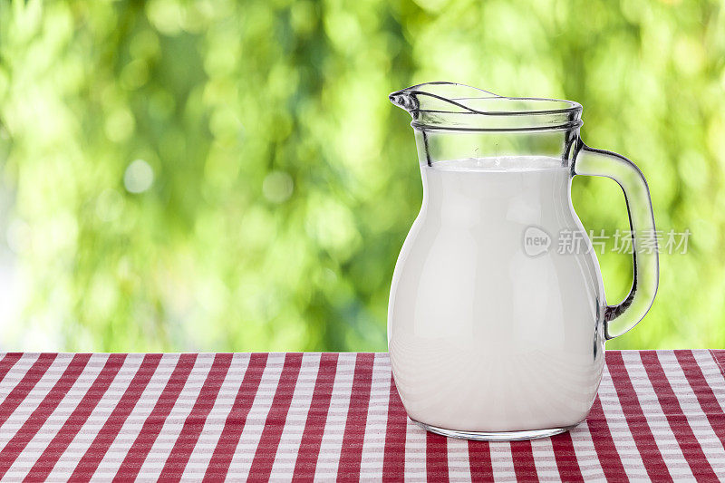 牛奶罐在红白格子桌布上对着散焦的绿色茂盛的树叶