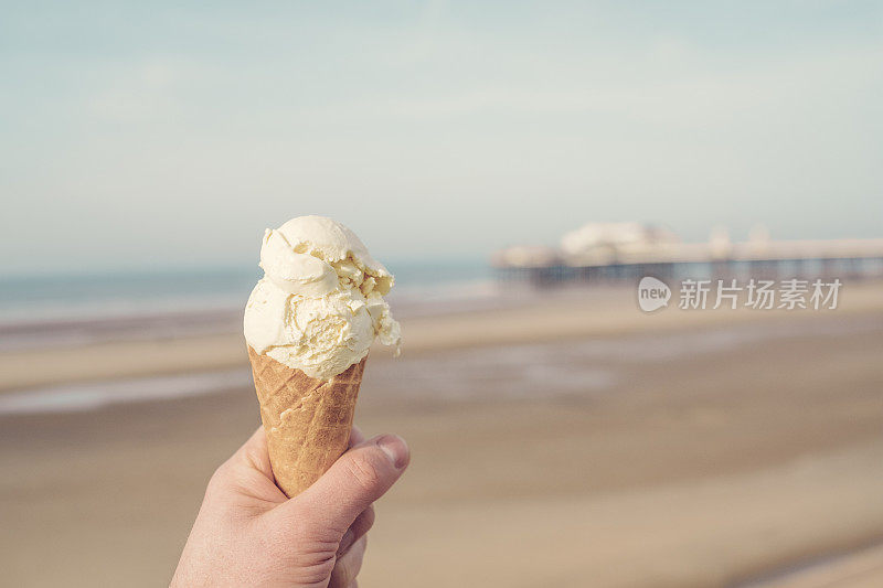 在一个阳光明媚的日子里，退潮时手拿冰淇淋蛋卷俯瞰布莱克浦的海滩。