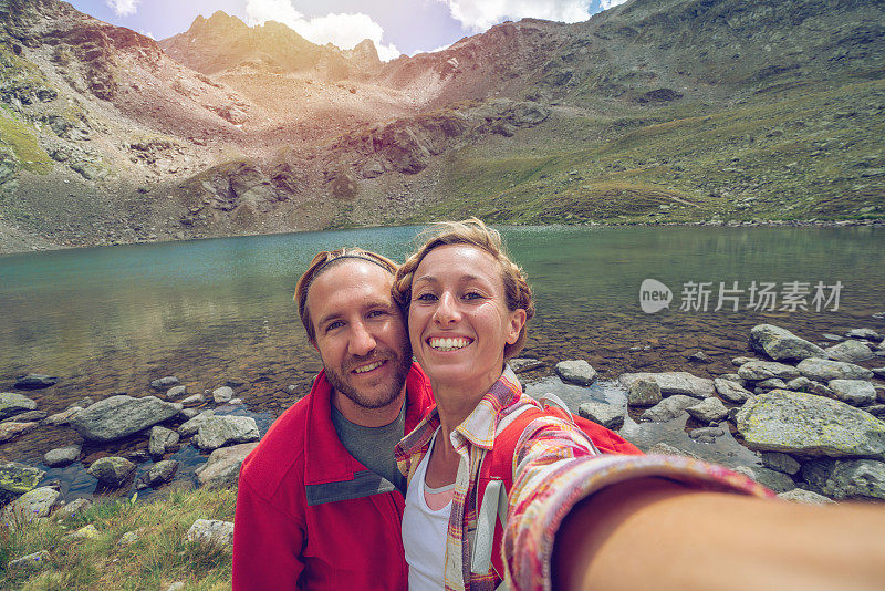 年轻的情侣徒步旅行在山湖边远足时拍自拍照