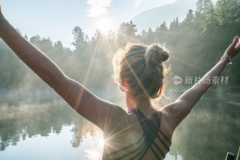 日出时分，一名年轻女子站在湖边的码头上，双臂张开