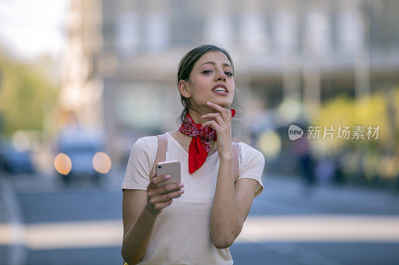 一名年轻女子正带着她的智能手机走在城市的路上