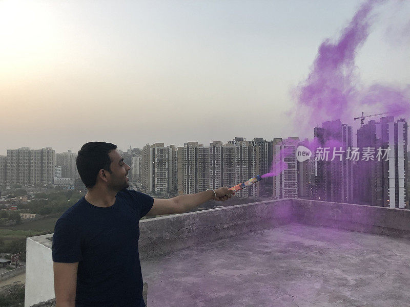 印度北方邦德里，一名印度男子在屋顶上释放彩色烟雾弹的照片