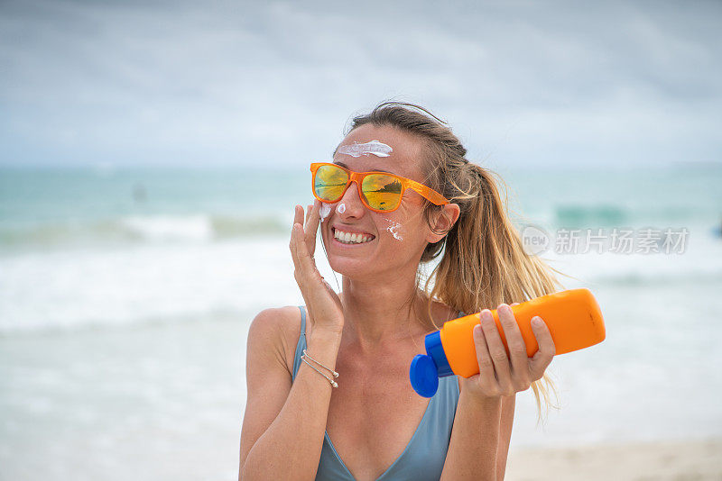 夏日――年轻女子在海滩上涂抹防晒霜，保护皮肤