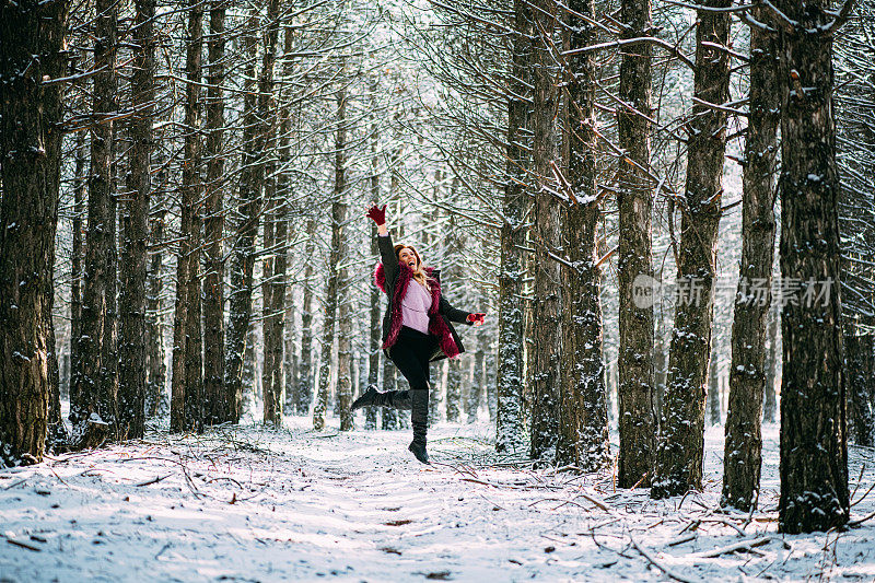 快乐的女人在雪域森林里跳跃