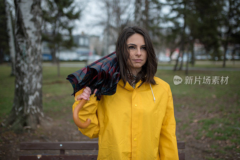 穿着黄色雨衣的年轻女子在公园里度过雨天