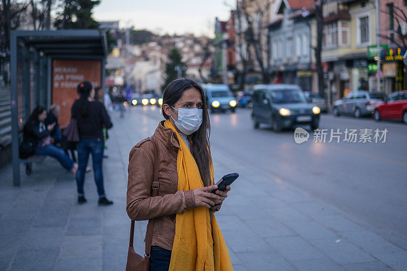 冠状病毒保护。妇女戴着口罩在城市里躲避传染病，下班后在等公交车。