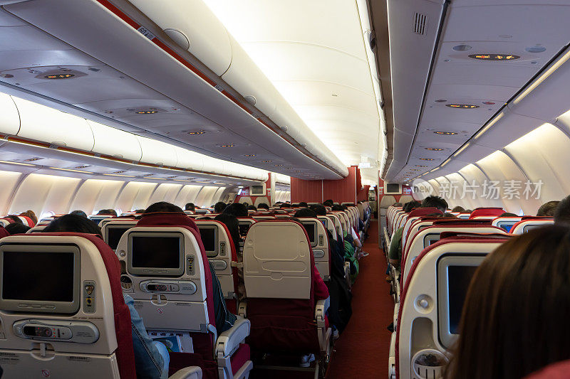 乘客座位，飞机内部，乘客坐在座位上，空姐在后面走过过道。