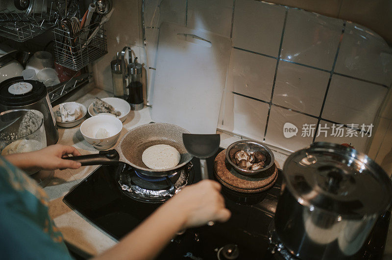 一位亚洲华人女性在厨房里用平底锅准备早餐煎饼