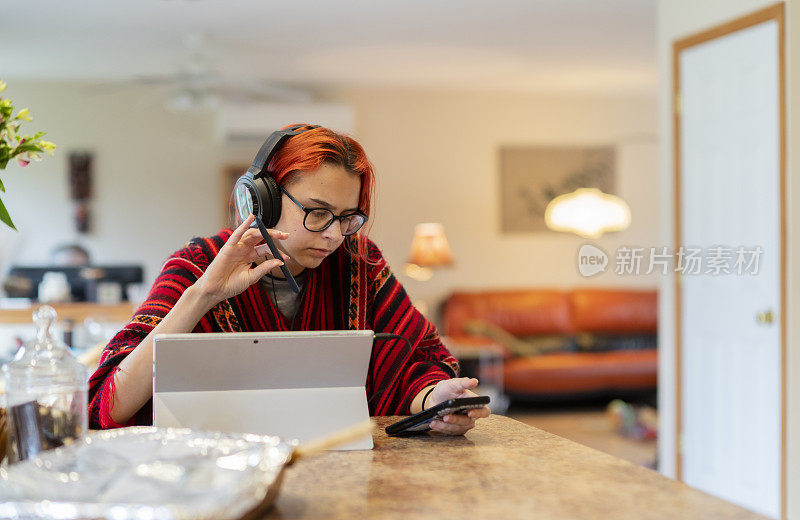 在新冠肺炎疫情导致的“呆在家里”的情况下，一名身穿披风、戴着耳机的少女正在远程上课，在厨房操作台使用笔记本电脑工作。