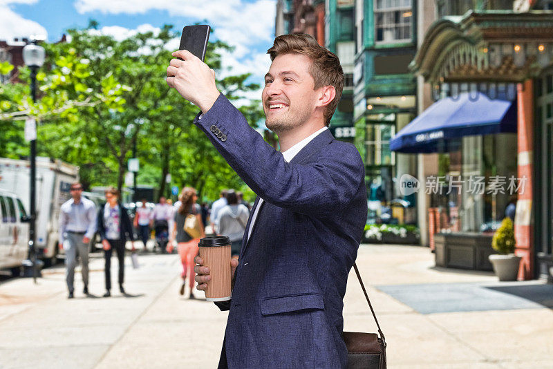 年轻男性摄影站谁是户外穿着商务服装，拿着咖啡杯和使用手机