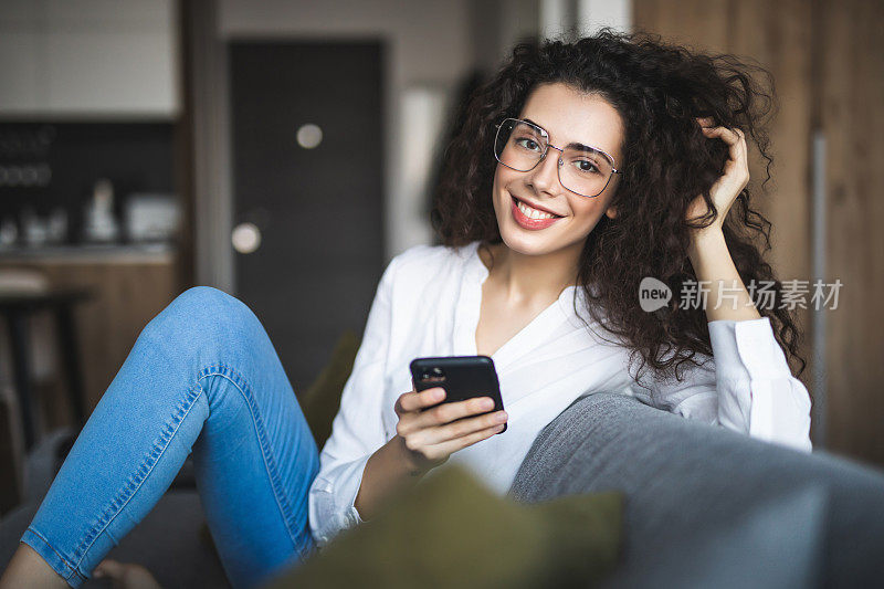 快乐的小女孩坐在家里的沙发上看智能手机短信