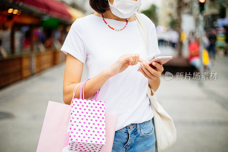 带着保护面罩的女人在购物时使用手机