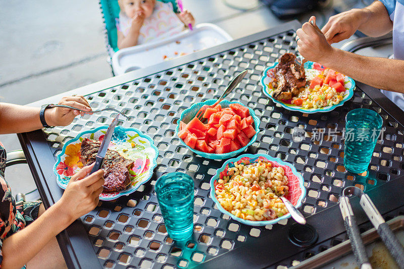 年轻的千禧一代父母和女孩子在露台餐桌上吃烧烤照片系列