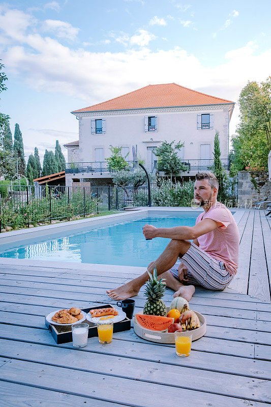 在法国阿尔代什有木制甲板和游泳池的法国度假屋。一名男子在法国南部的度假屋享受豪华假期期间，在泳池边的木甲板上放松