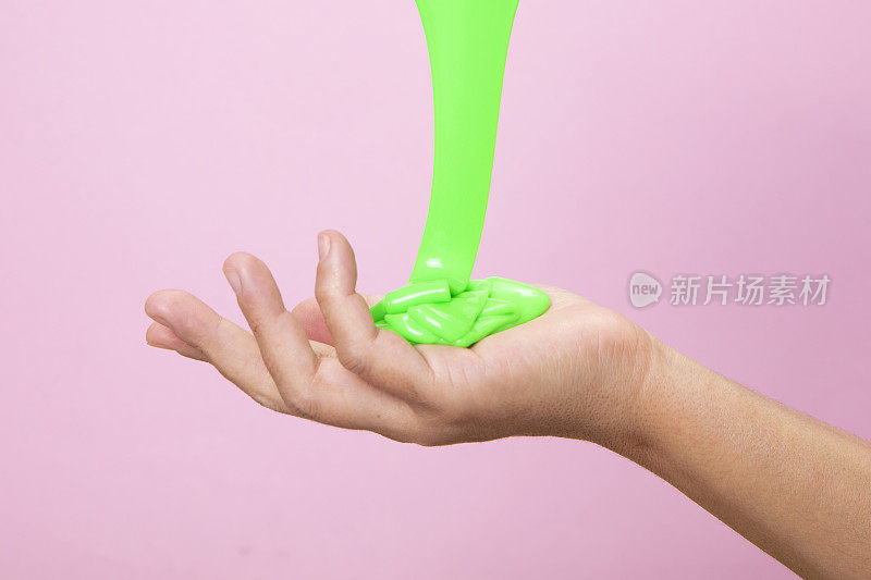 手拿着一些东西与霓虹灯绿色黏液玩具在粉红色波普艺术背景。