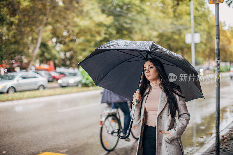 一个雨天，在公共汽车站带着雨伞的女人