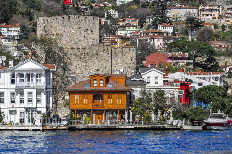 在土耳其伊斯坦布尔市，房子和防御墙在海滨和一艘船漂浮在博斯普鲁斯海峡的水上。