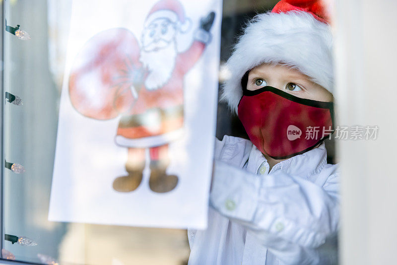 2019冠状病毒病大流行期间，一名小男孩在家里窗户上贴圣诞画