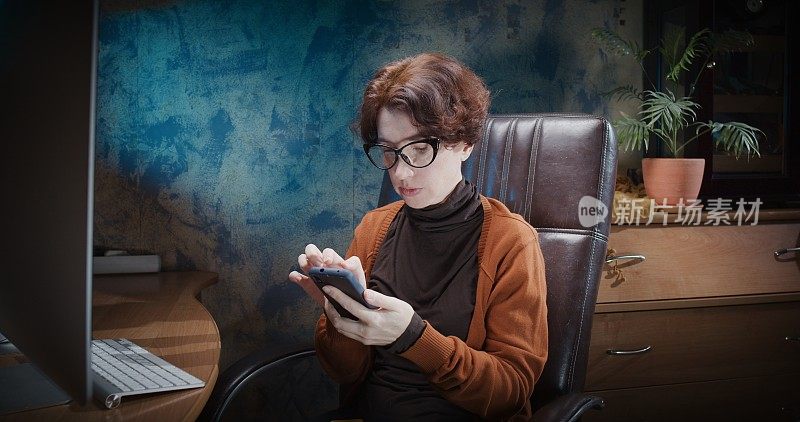 成熟的女人会一边在电脑桌前工作，一边玩智能手机