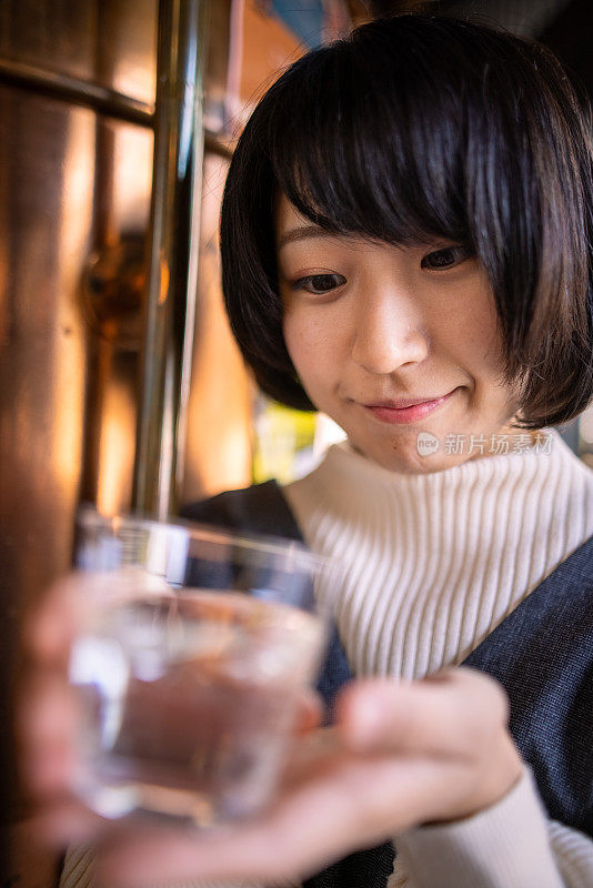 在传统的日本温泉区，快乐的年轻女子拿着一杯“saki”(日本米酒)