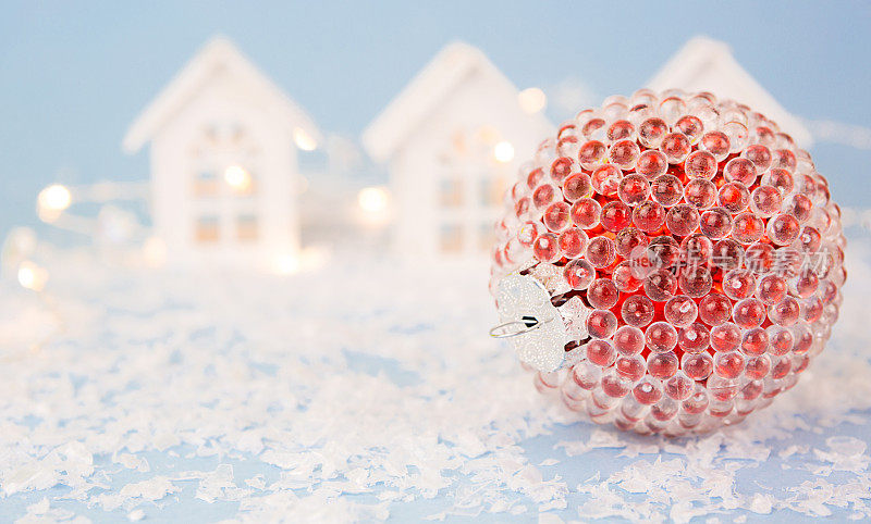红色圣诞球在蓝色的背景与人造雪和灯的花环在散景。喜庆的背景，新春的喜庆。副本的空间。白色的小木屋，街道上有模糊的房子