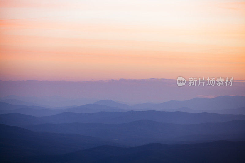 起伏的山丘与柔和的桃红色和粉红色的天空在日落的山上