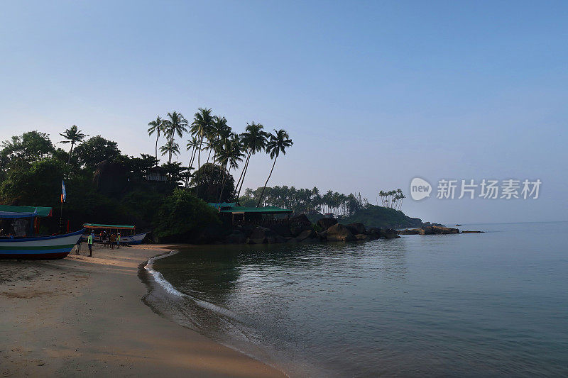 印度热带海滩的形象，与游客的冬季度假日光浴，在沙滩上散步，在大海中游泳，海岸线与异国情调的高大椰子树，度假的度假者与蓝天背景的帕洛伦海滩，印度果阿