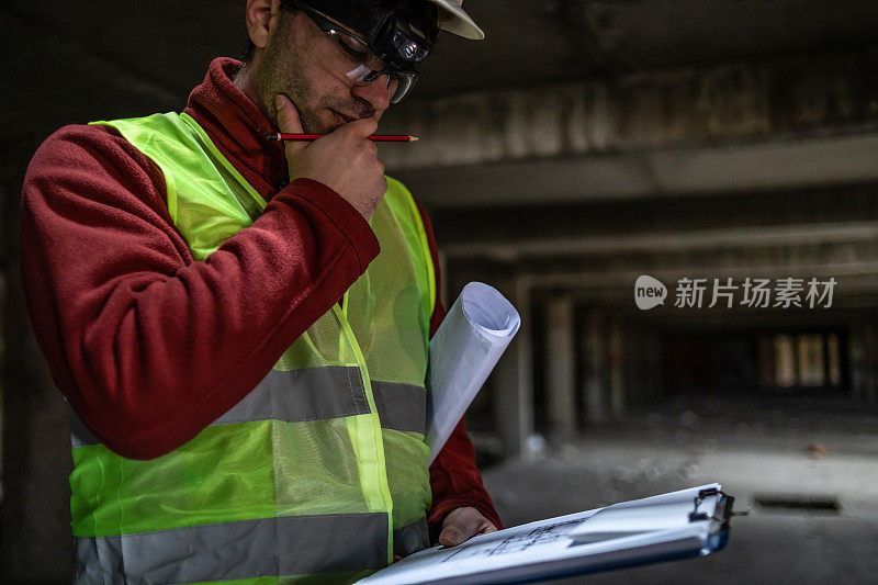 工程师在施工现场阅读平面图的肖像。一位戴着安全帽、穿着安全背心的土木工程师正在使用数码平板电脑。致力于建筑改造和投资评估。