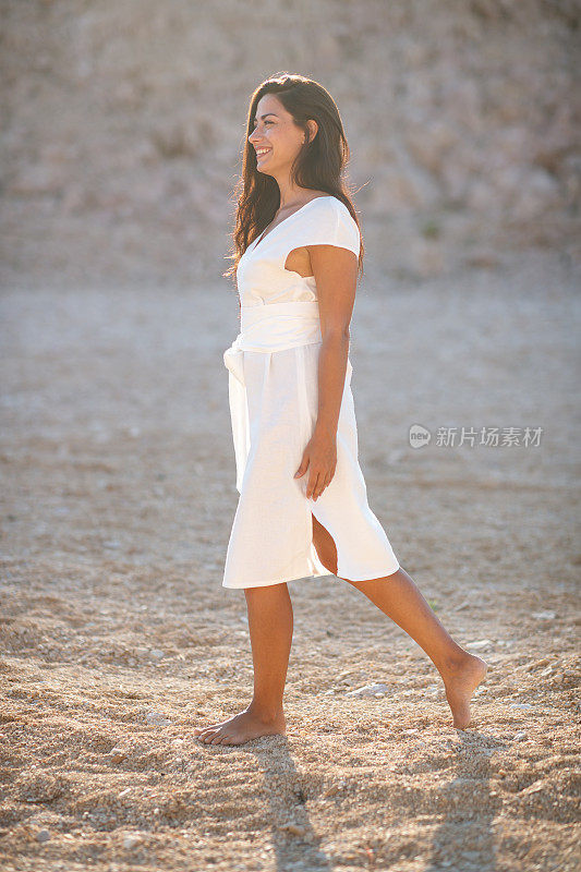 穿着白色夏装的美丽女子微笑着独自行走在石头沙漠中