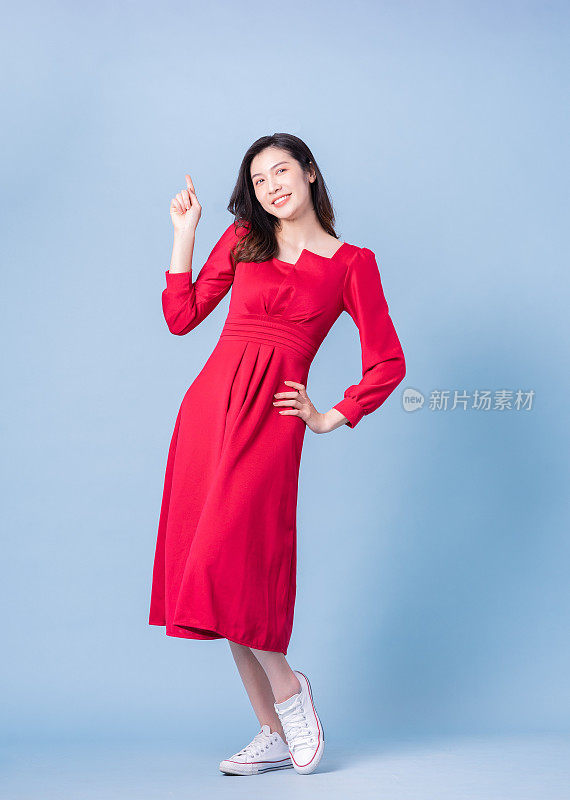 穿着蓝色背景的红色连衣裙的年轻亚洲妇女的全长图像