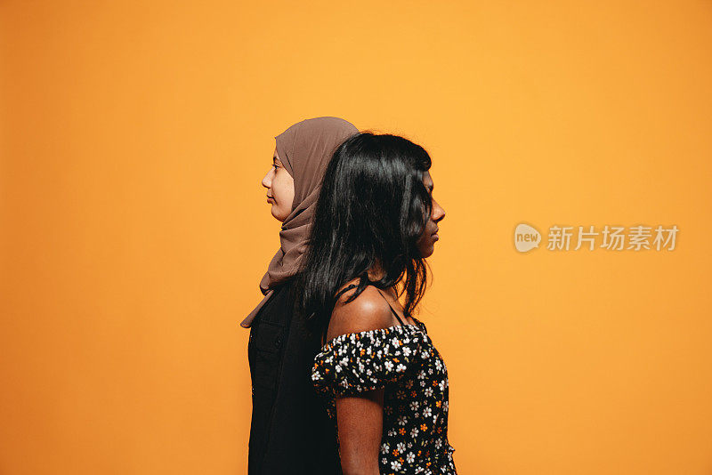 桔色背景下的两个年轻成年女性的侧视图